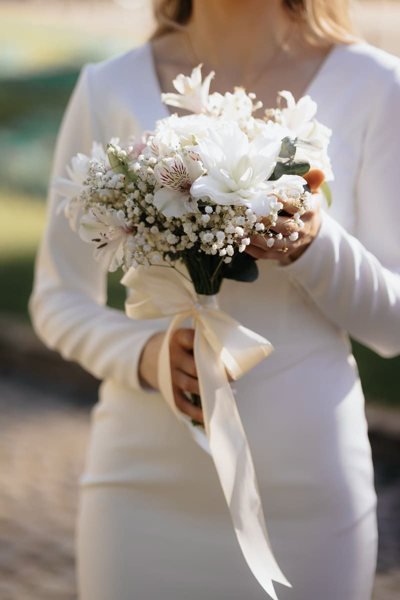Mireasă în rochie albă ținând un buchet alb cu panglici lungi